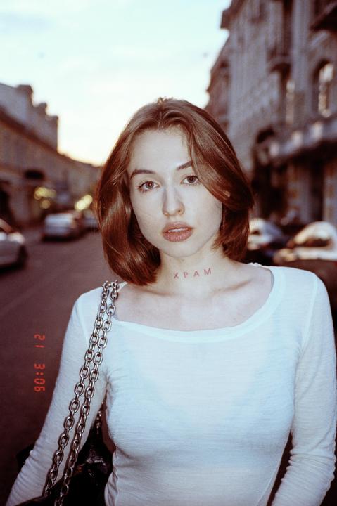 A woman with a tattoo on her neck stands on a street at dusk.