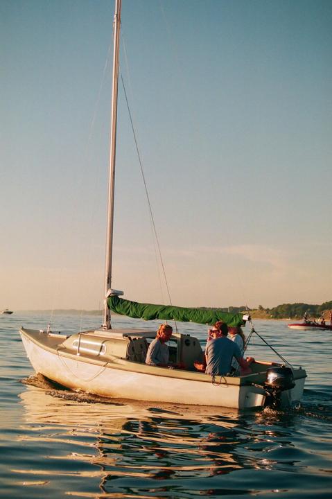 A small sailboat with four people on board moves across the water at golden hour.