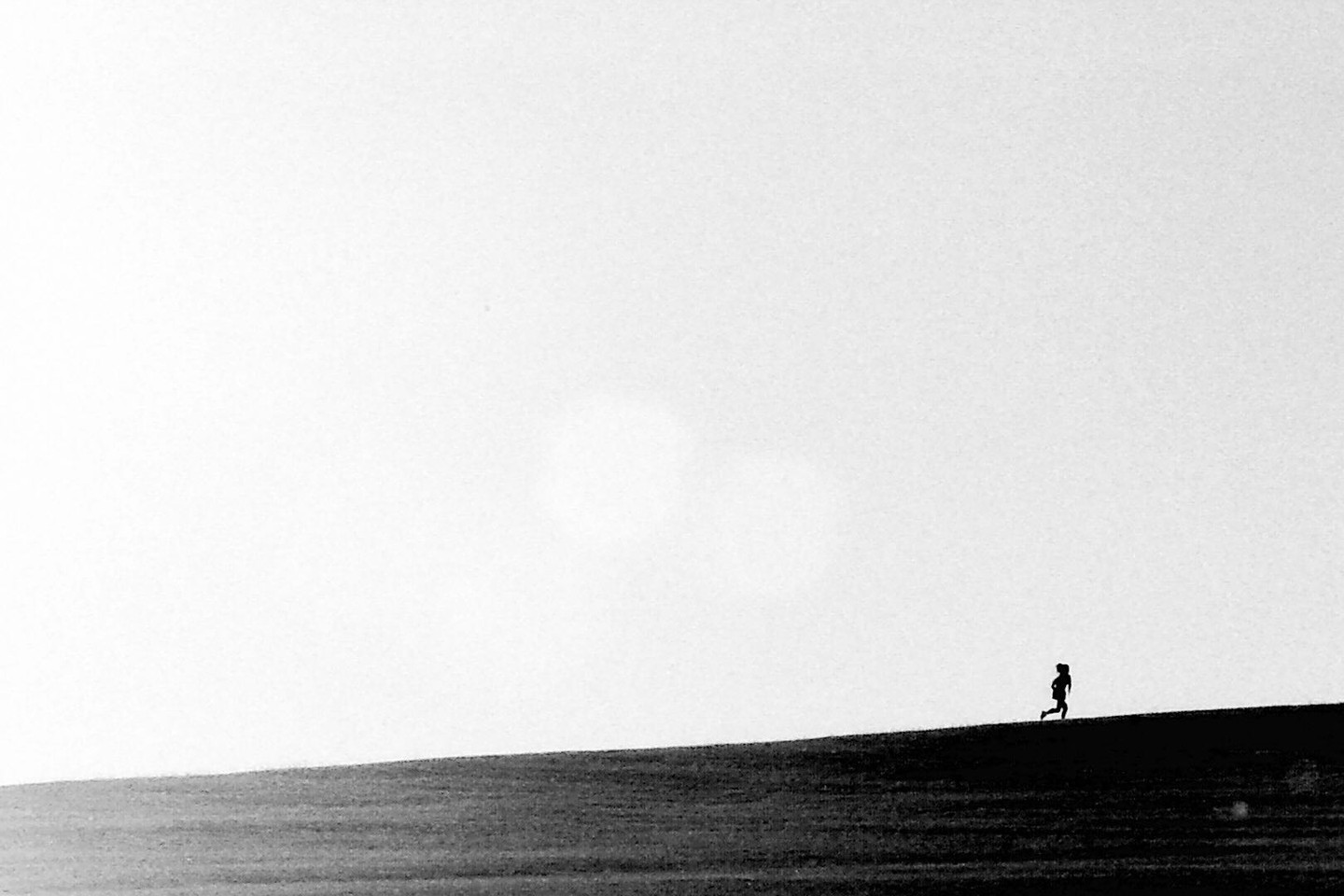 A lone jogger is silhouetted against a bright sky as they run up a hill.