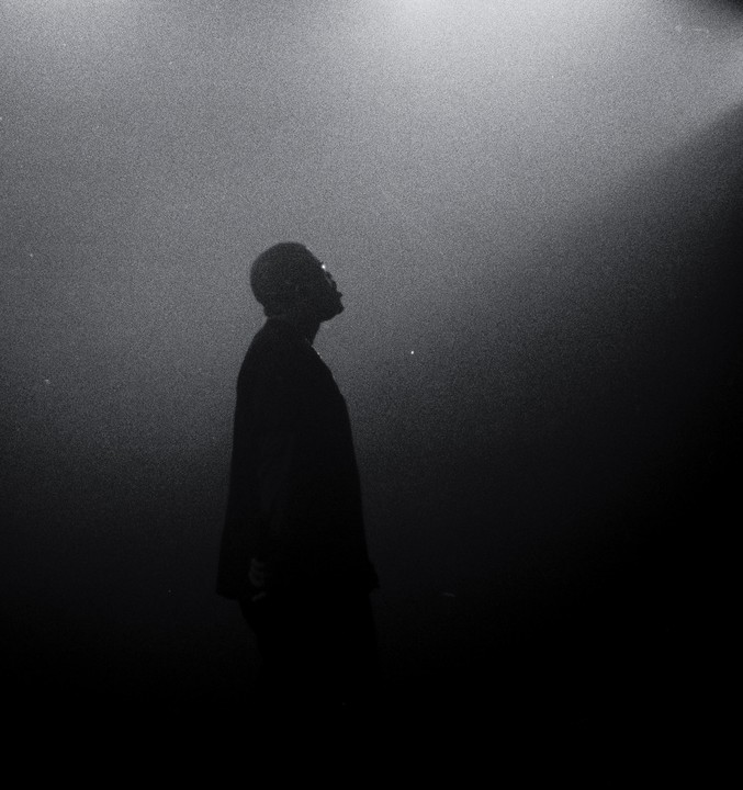 A man in silhouette looks up into a bright spotlight.