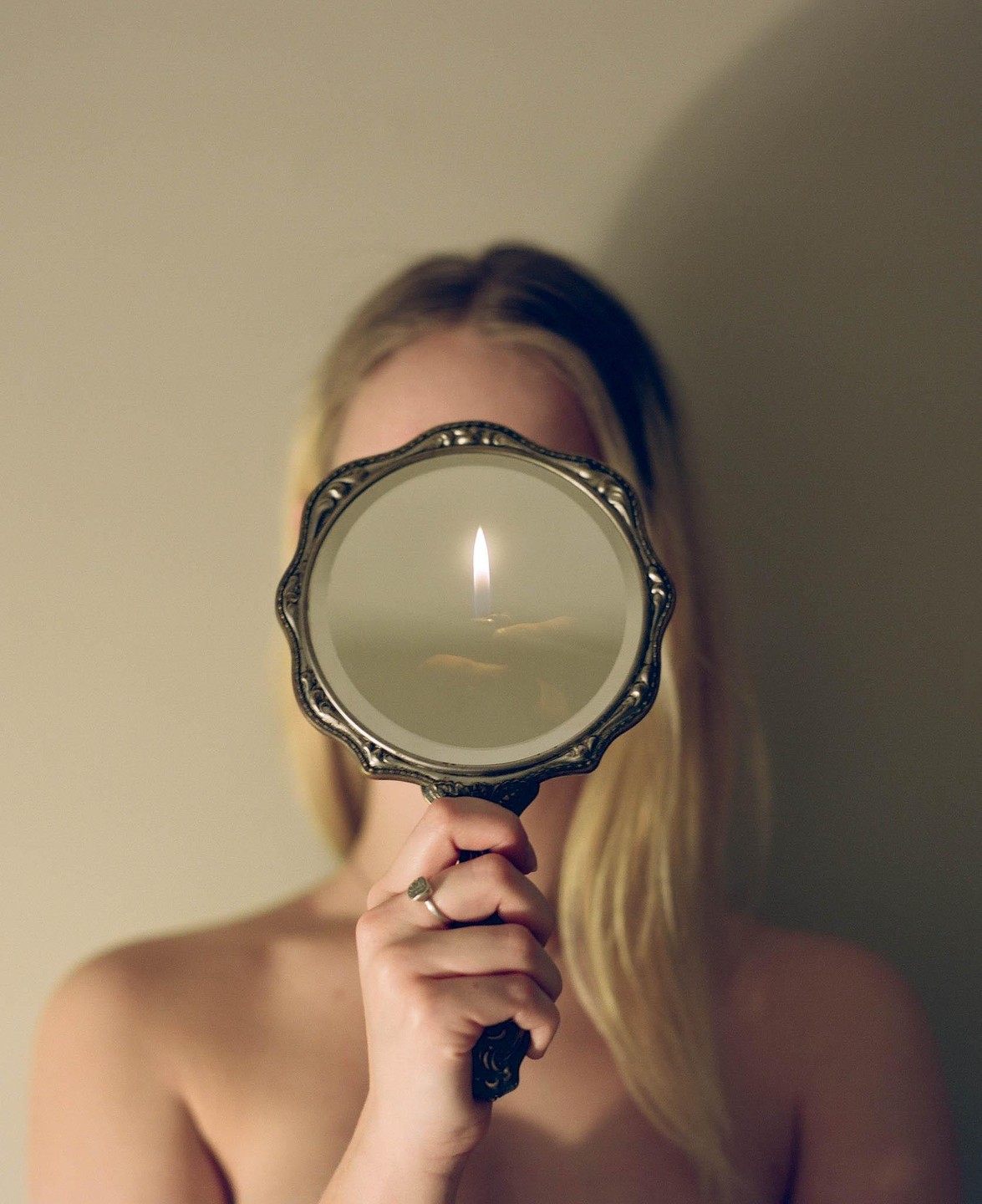 A woman holds a handheld mirror reflecting a lit candle in front of her face.