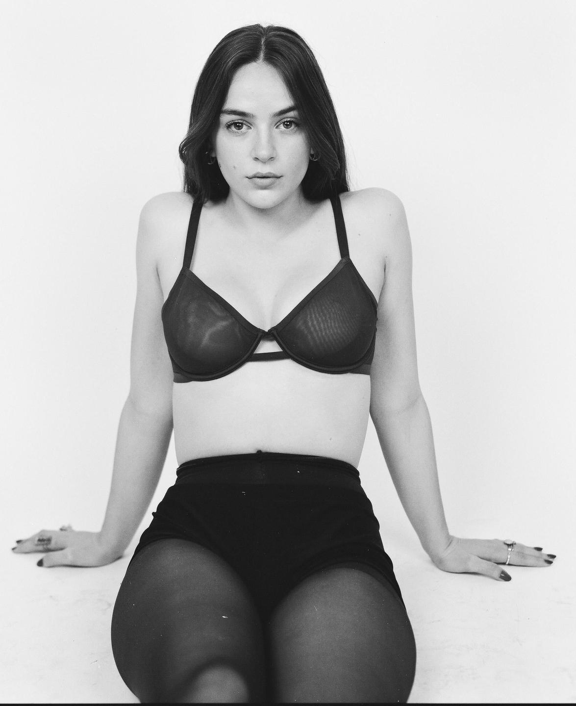 A woman wearing a bra and shorts sits on a white surface.