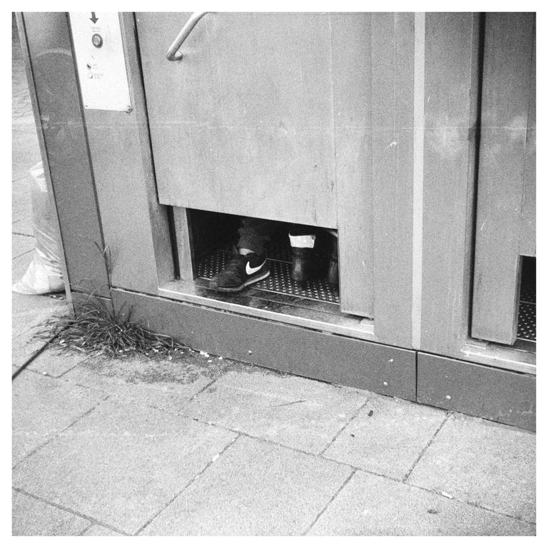 A person's feet are visible inside a public toilet stall.