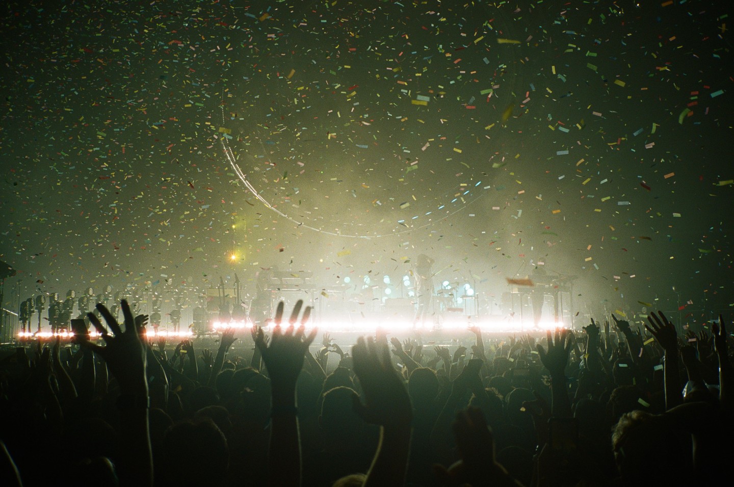 Confetti falls over a crowd with their hands raised at a concert.