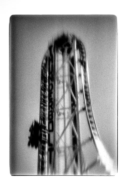A blurry black and white image shows a roller coaster with a car at the top of a drop.