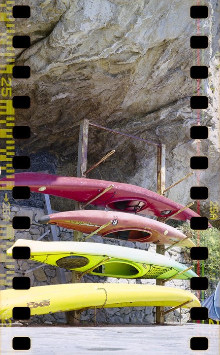 Four colorful kayaks are stored on a metal rack against a rocky cliff face.
