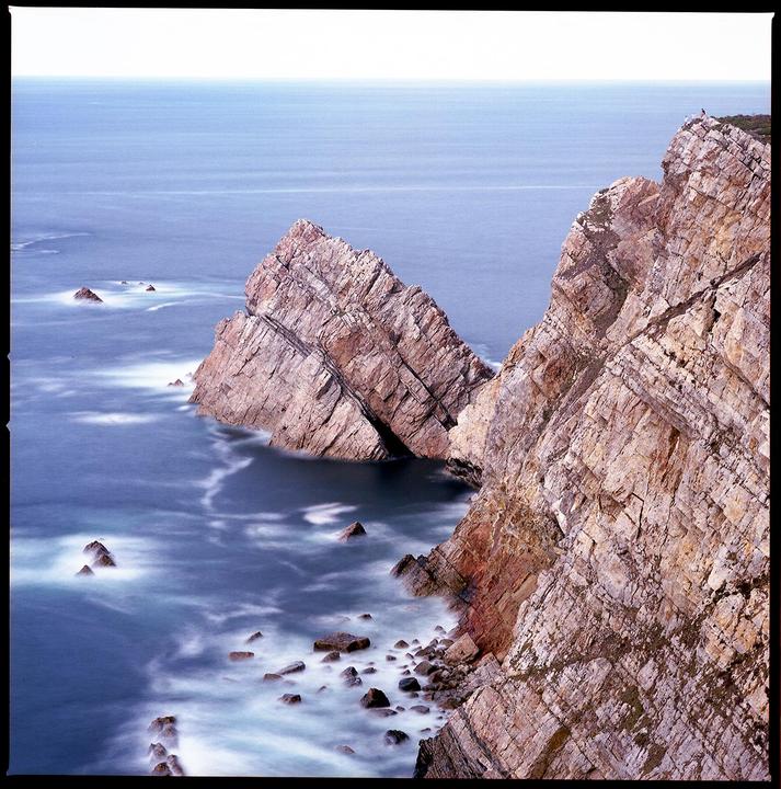 The ocean meets a rocky coastline with a long exposure blurring the water.