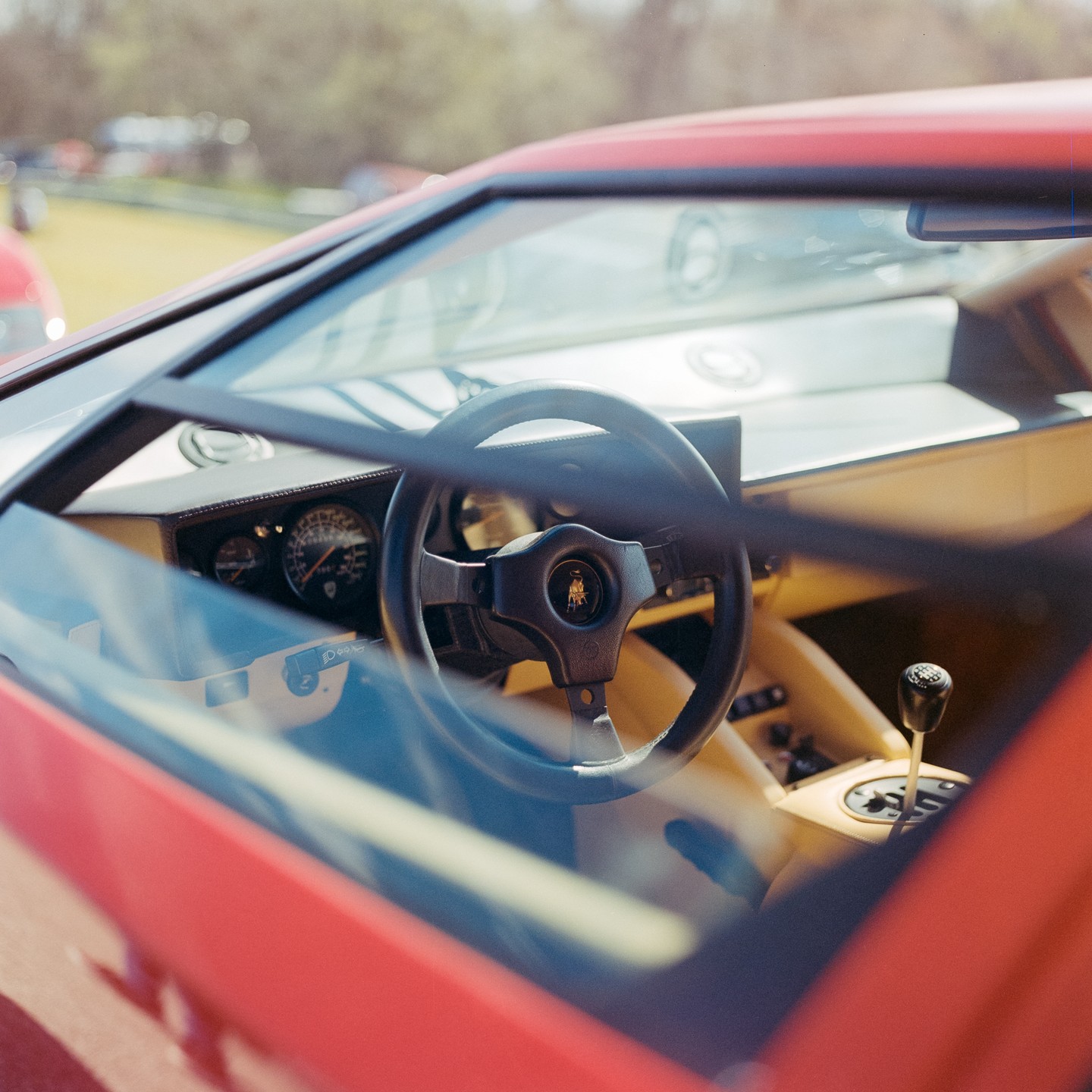 The interior of a red Lamborghini Countach is visible through the windshield and side window, showing the steering wheel, dashboard, and gear stick.