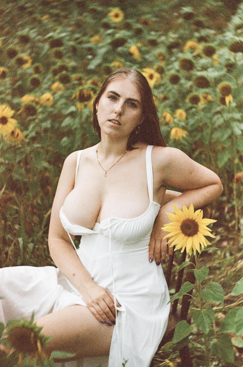 A woman in a white dress sits in a field of sunflowers.