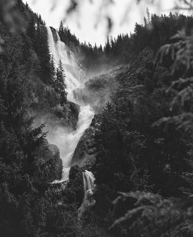 A powerful waterfall cascades down a rocky, forested mountainside, creating mist at its base.