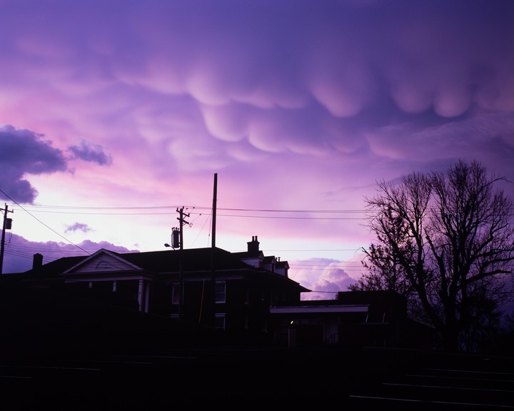 A dramatic purple sky with mammatus clouds hangs over silhouetted buildings and a bare tree.