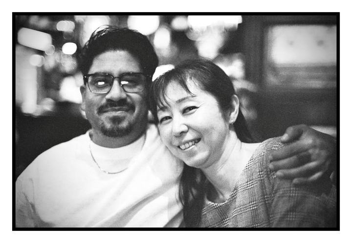 A man and a woman are smiling at the camera, with the man's arm around the woman.