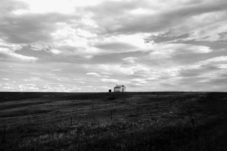 A small house stands alone on a grassy plain under a cloudy sky.