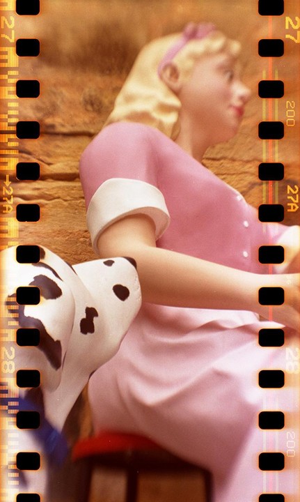 A blonde doll in a pink dress sits next to a dalmatian toy.