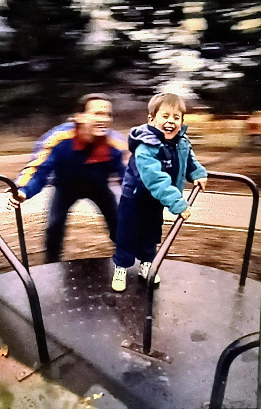 A man and a child are on a merry-go-round, with the child in the foreground laughing.