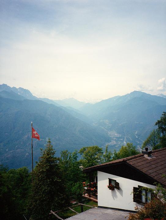 A Swiss flag flies next to a house overlooking a mountain valley.