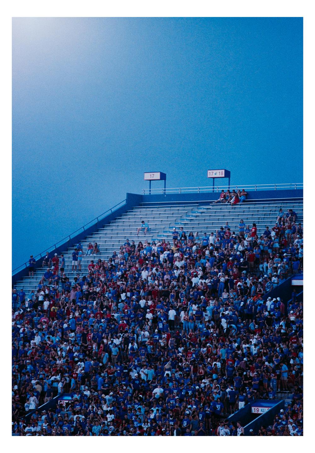 A large crowd of people are seated in a stadium under a bright blue sky.