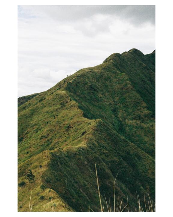 A mountain ridge covered in green grass extends under a cloudy sky.
