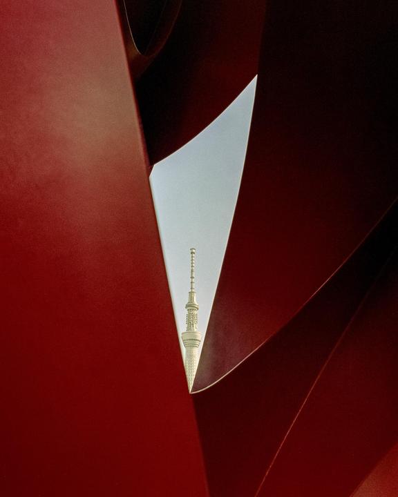 A tall white tower is visible through a triangular opening in a red structure.