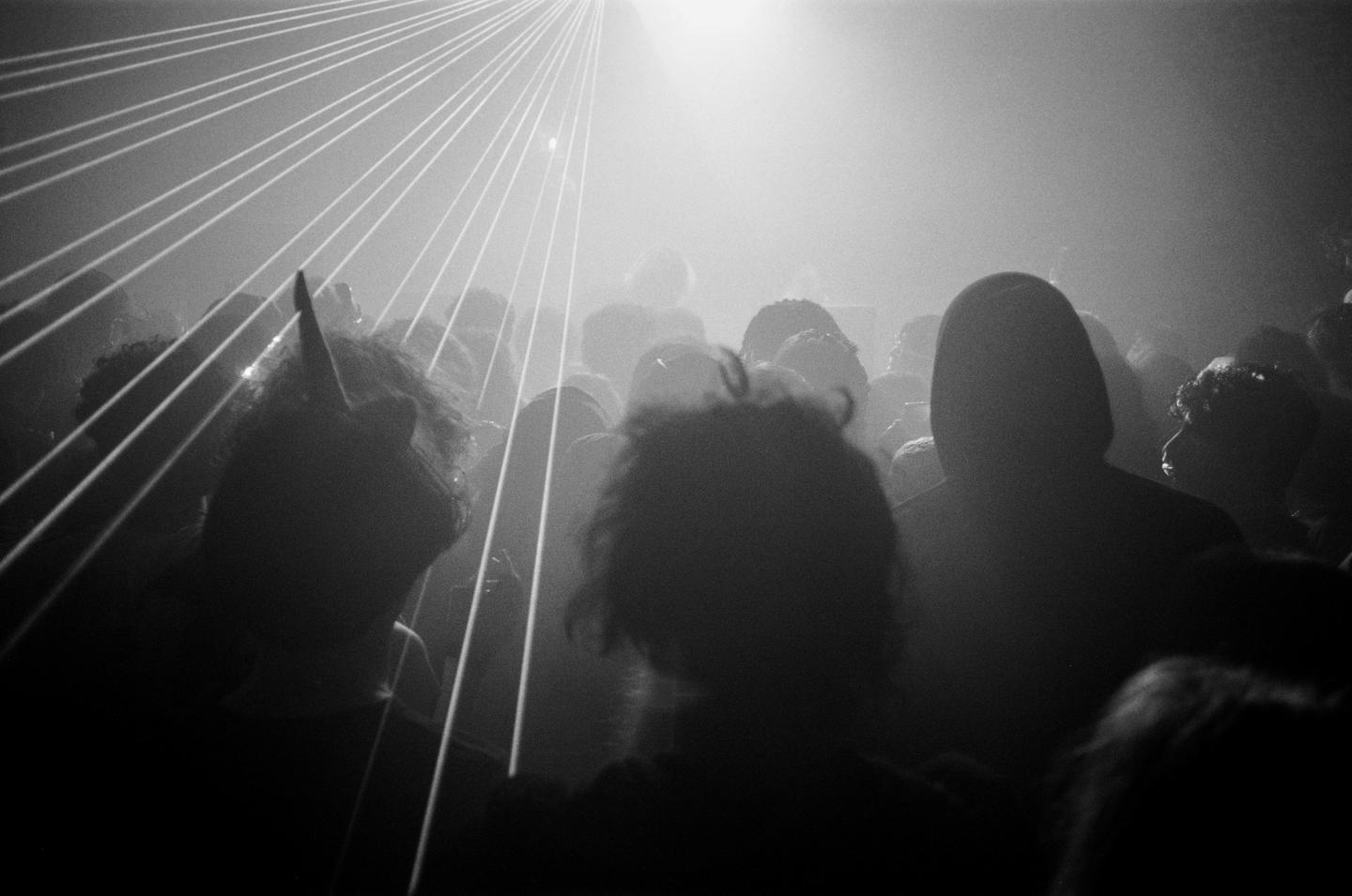 A crowd of people are silhouetted by bright lights and laser beams.
