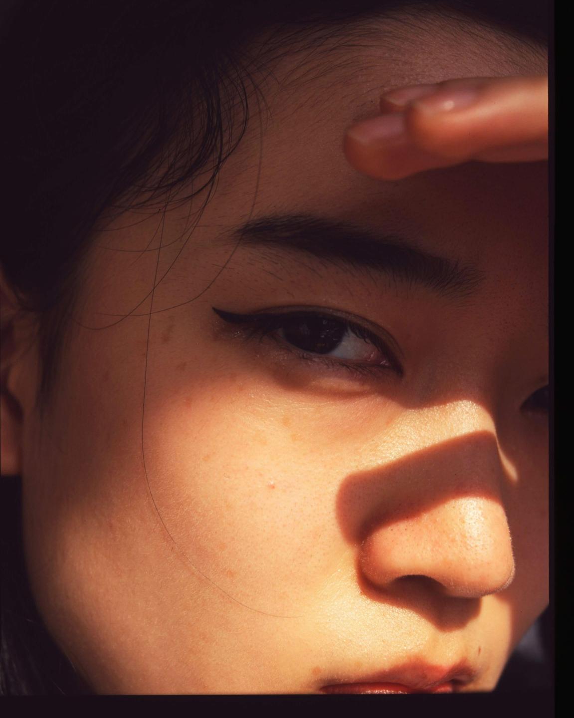 A woman's face is partially obscured by shadow as she shields her eyes from the sun.