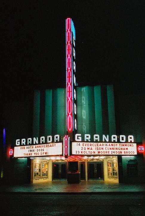 A movie theater with a large neon sign and marquee is illuminated at night.