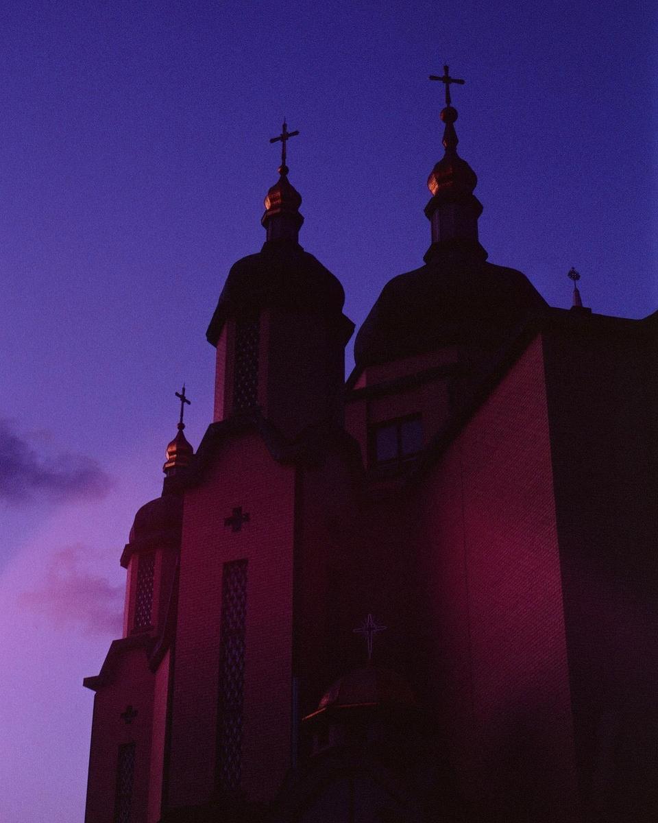 A church with multiple domes and crosses is silhouetted against a purple and pink sky.