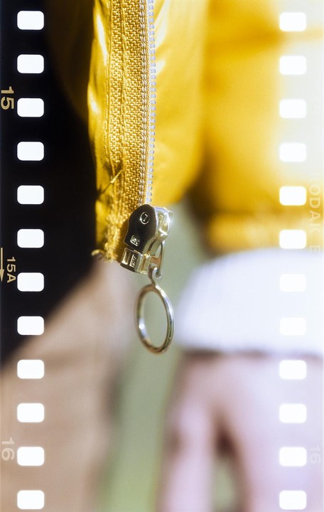 A zipper on a yellow jacket is shown in close-up with a film border on the left.