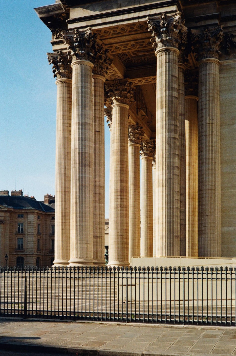 A black metal fence stands in front of a large stone building with many tall columns.