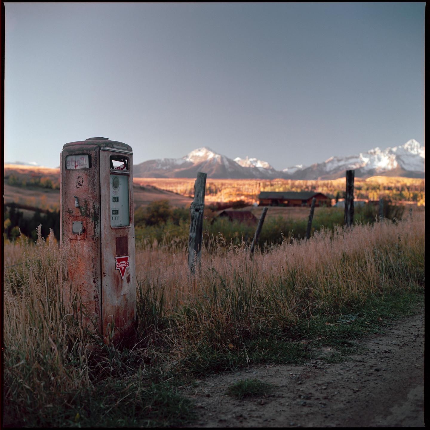 An old gas pump stands in a field of tall grass with mountains in the background.