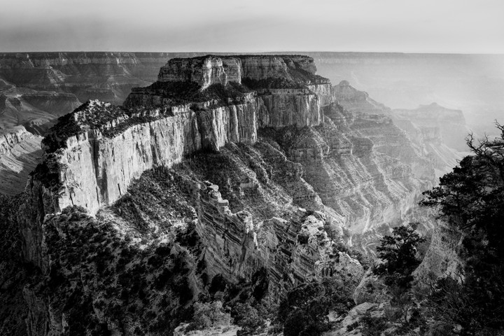 A vast canyon landscape with layered rock formations and sparse vegetation is visible under a hazy sky.