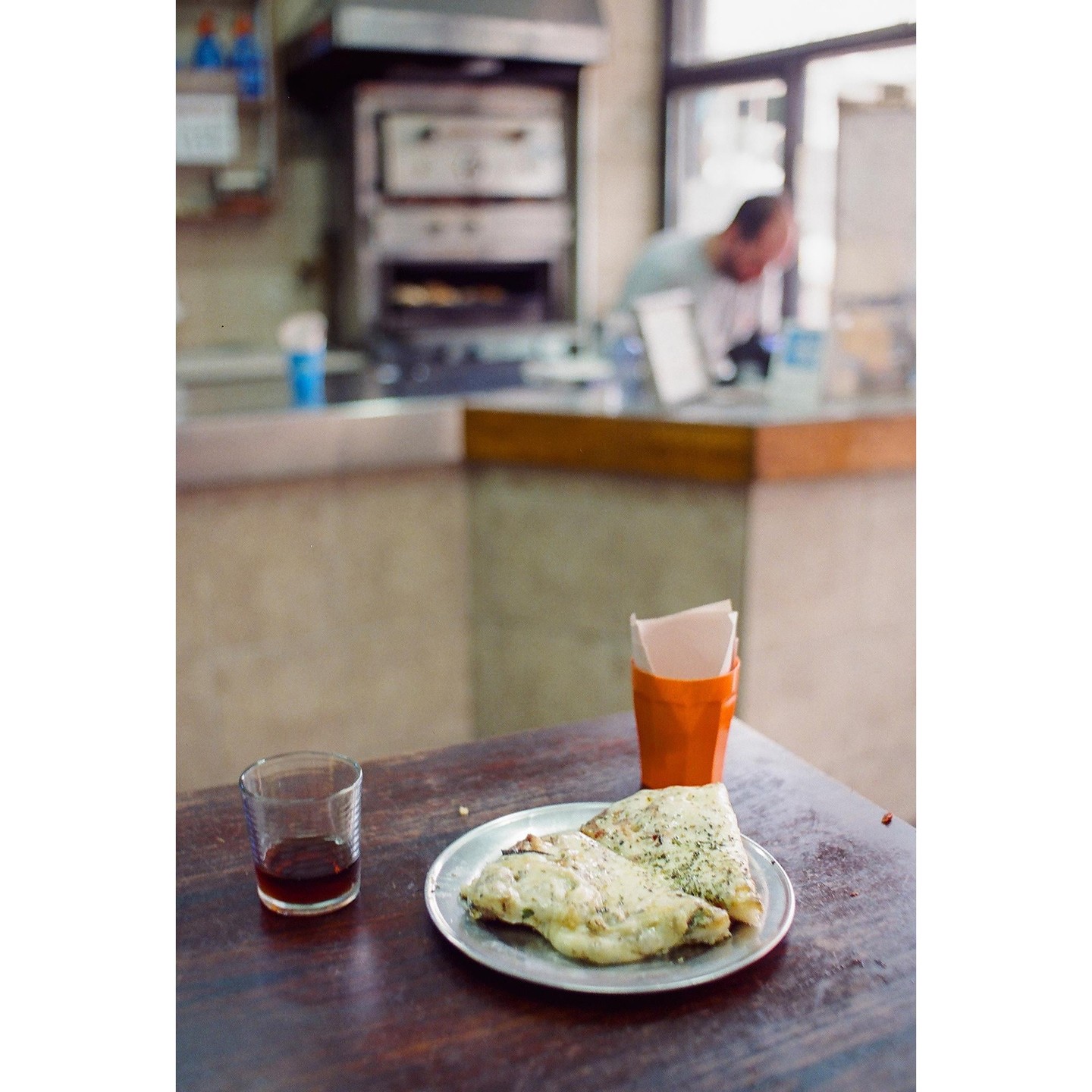 Two slices of pizza and a glass of red wine sit on a wooden table in a pizzeria.