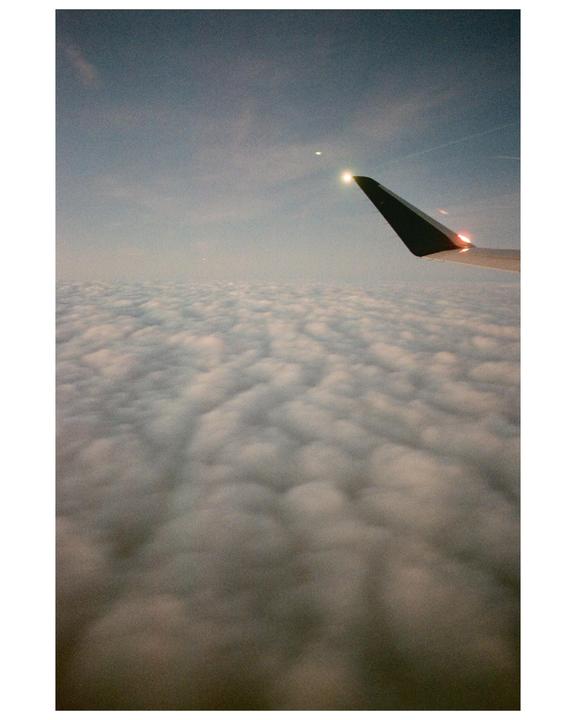 An airplane wing is visible above a vast expanse of clouds under a hazy sky.