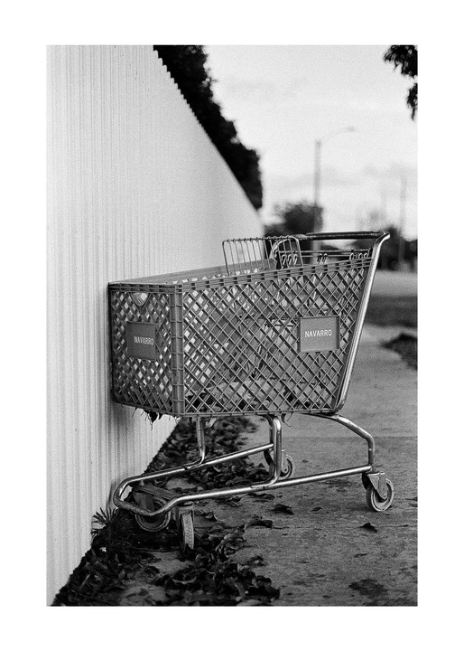 A shopping cart with the name "Navarro" on its side is parked next to a white wall on a street.