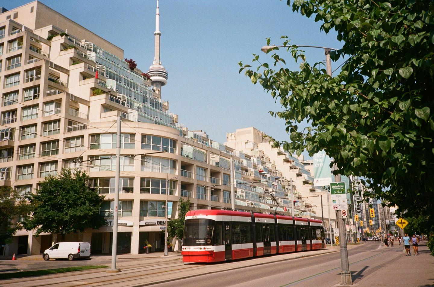 A red and white streetcar travels along a city street with a tall building and tower in the background.