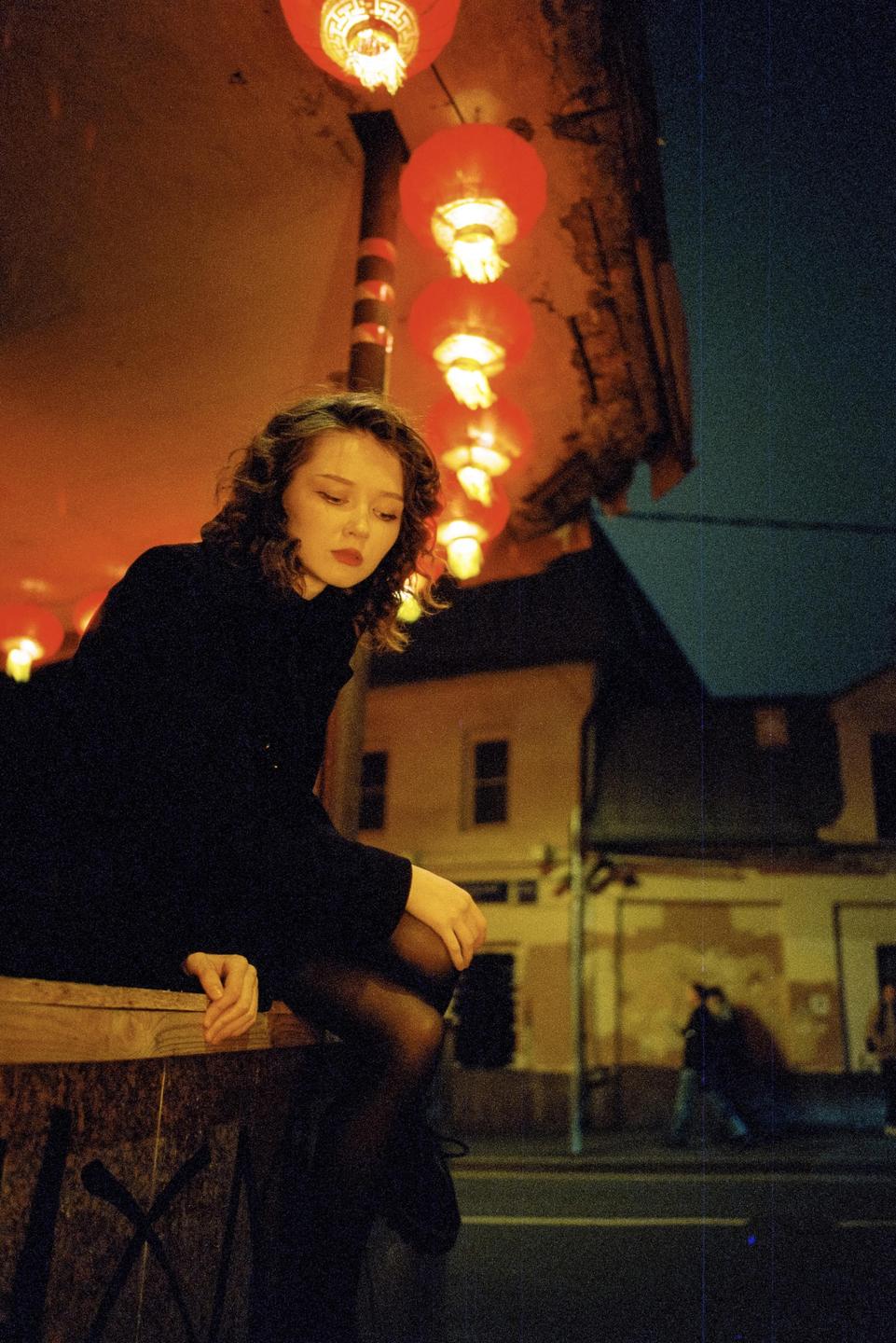 A woman sits under a row of red lanterns at night.