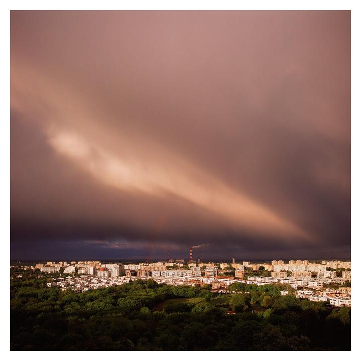 A dramatic sky with a shaft of light illuminates a city with many buildings and green trees.