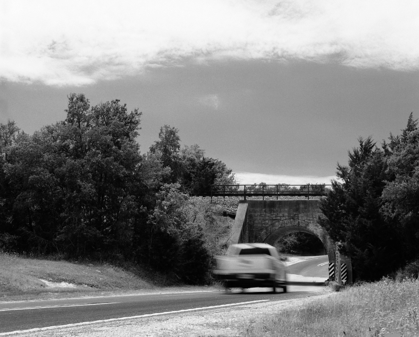A blurry car drives on a road towards a tunnel under a stone bridge.