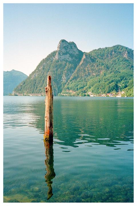 A wooden post stands in a lake with mountains and a small village in the background.