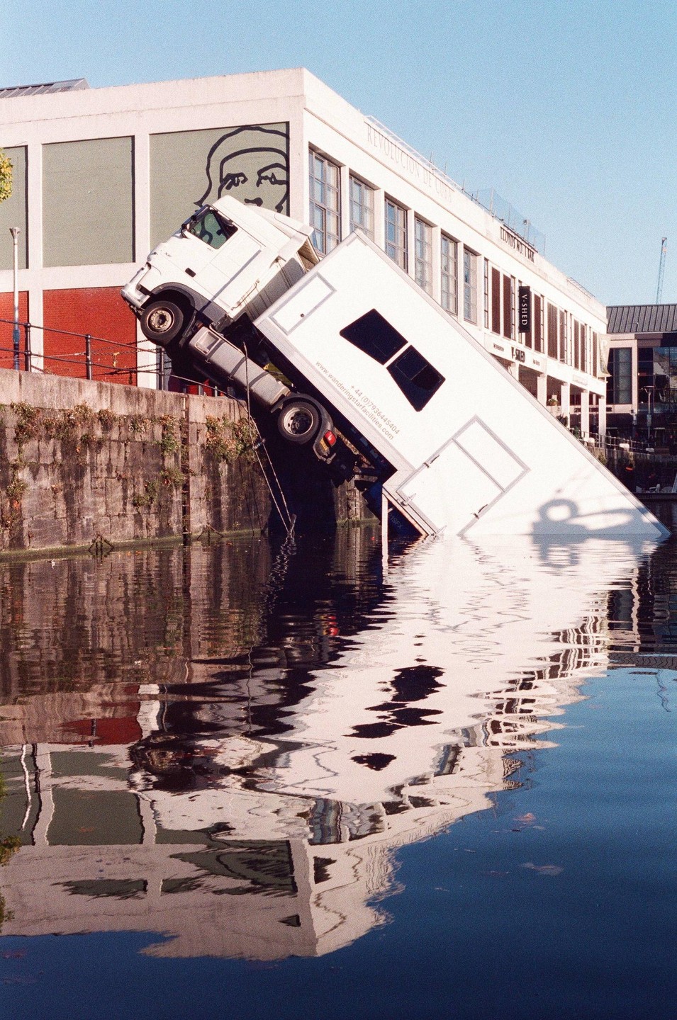 A white truck is partially submerged in water next to a building with a mural.
