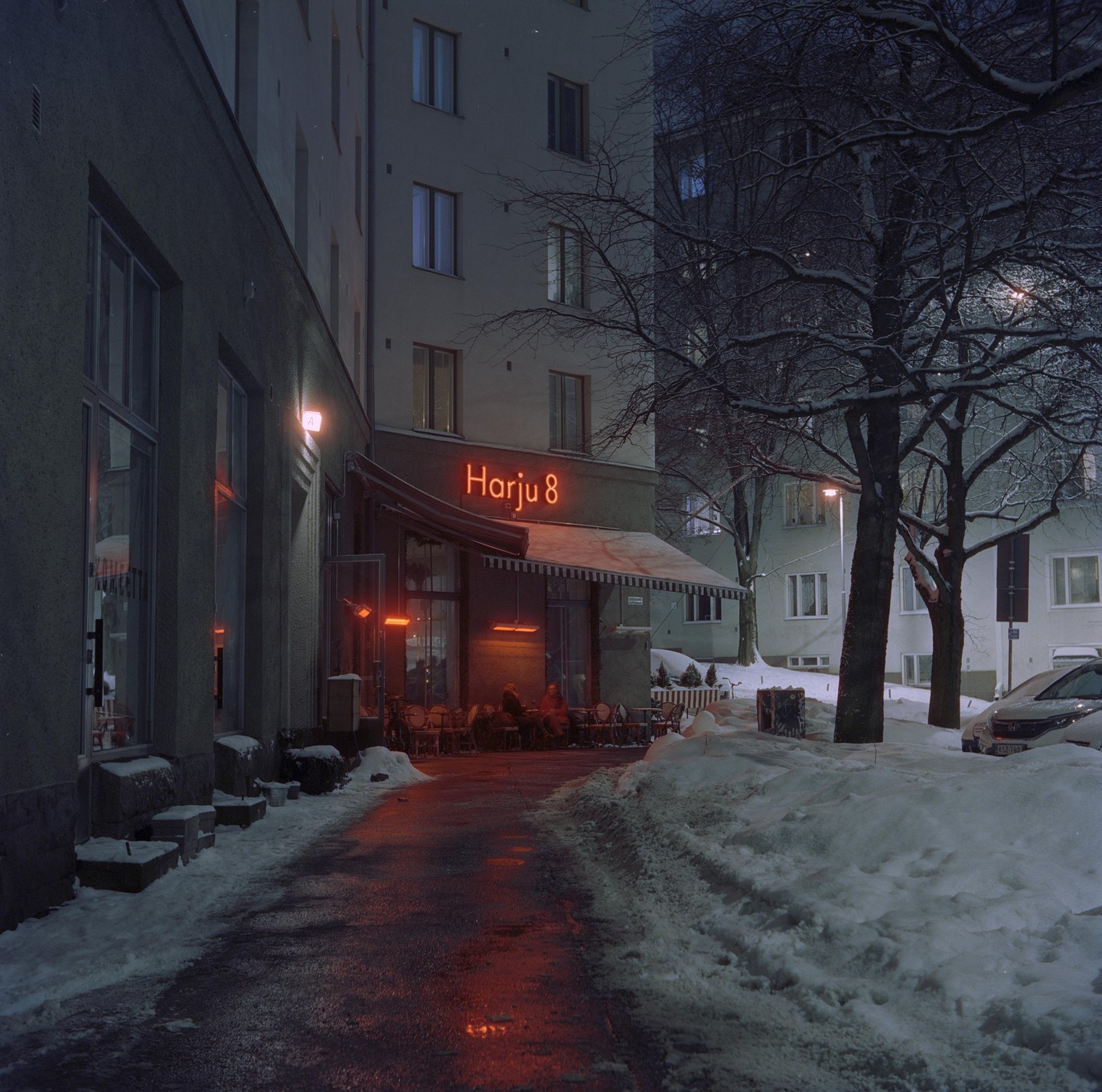 A restaurant terrace with a neon sign is visible at night, surrounded by snow and bare trees.