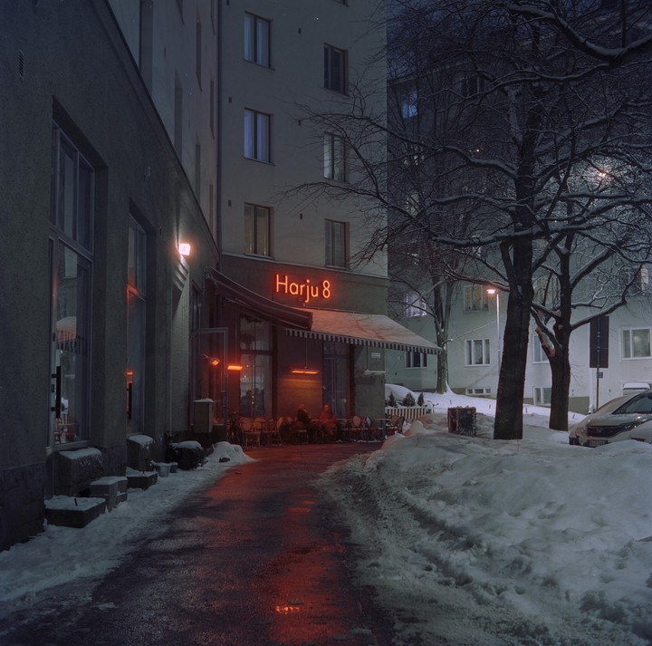 A restaurant terrace with a neon sign is visible at night, surrounded by snow and bare trees.