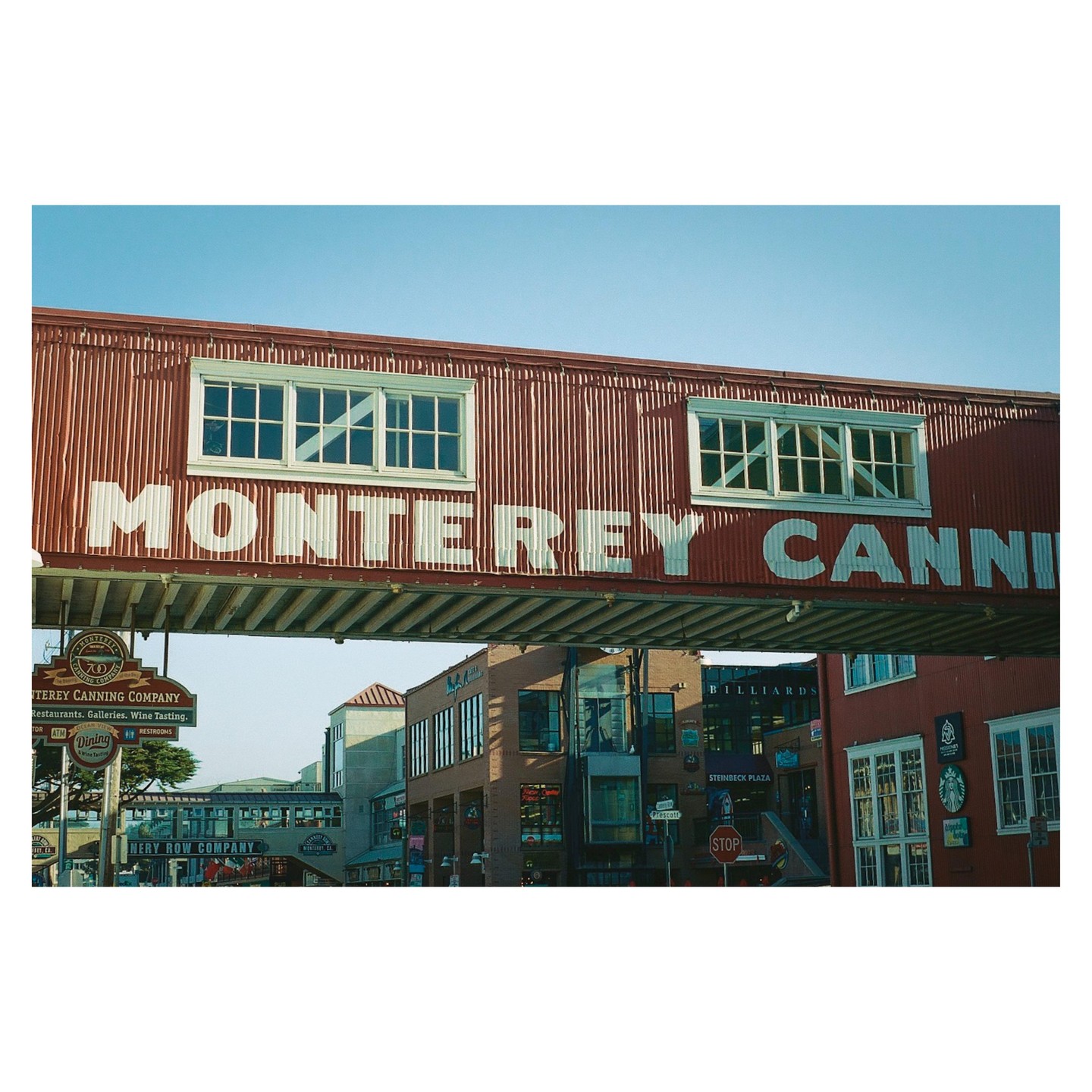 A red corrugated metal building with "MONTEREY CANNING COMPANY" written on it spans across a street with other buildings visible below.