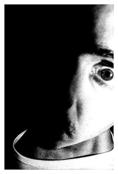 A high-contrast black and white self-portrait shows a man's face with one eye visible and the other side of his face in shadow.