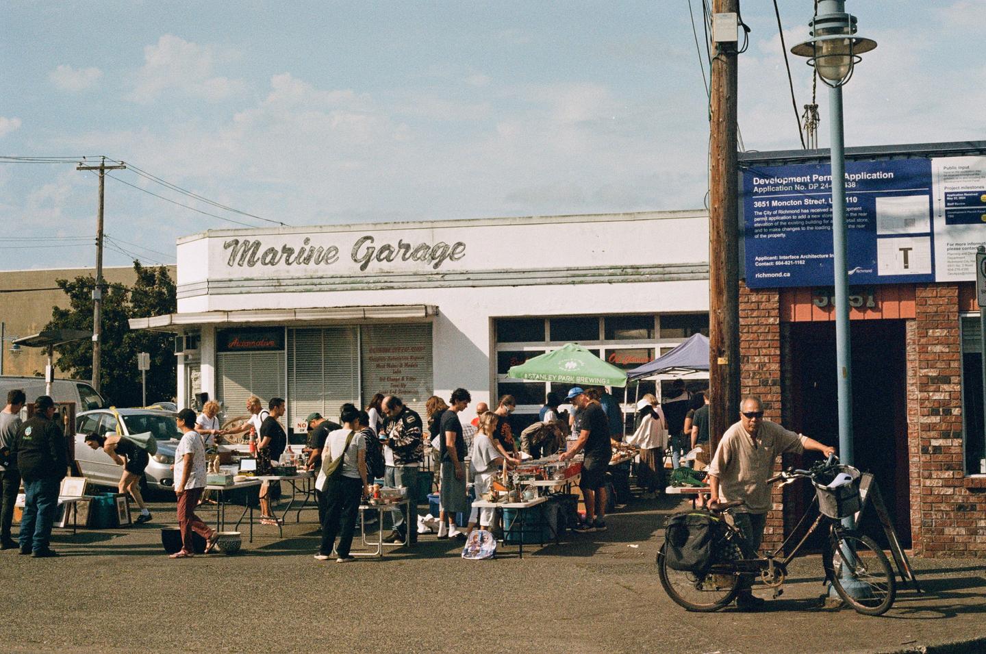 A street market is taking place in front of the Marine Garage building, with many people browsing items on tables.
