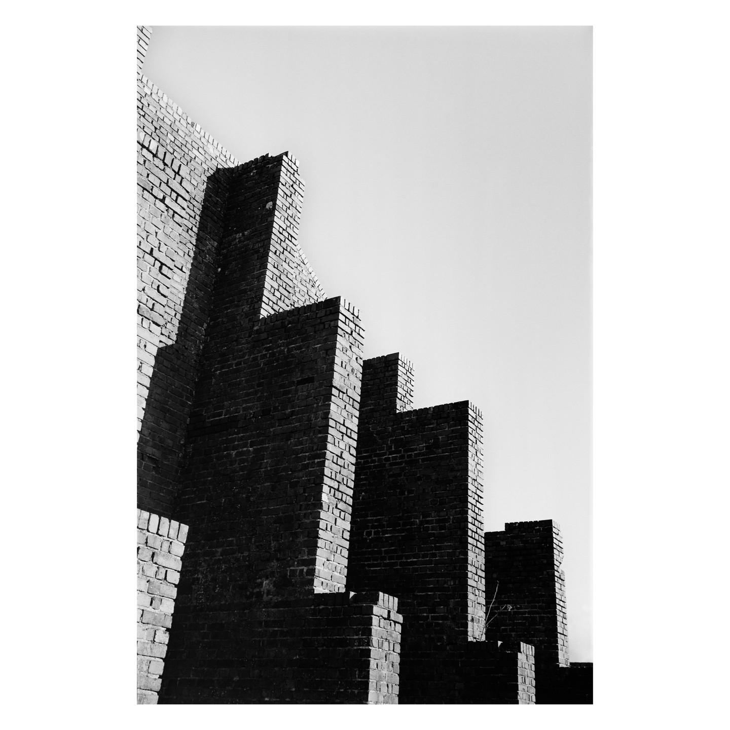 A series of brick walls of varying heights are silhouetted against a bright sky.