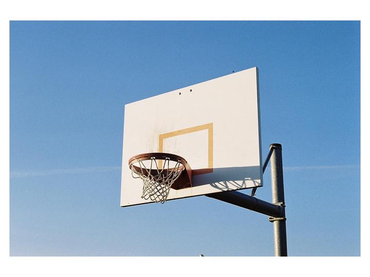 A basketball hoop and backboard are visible against a clear blue sky.