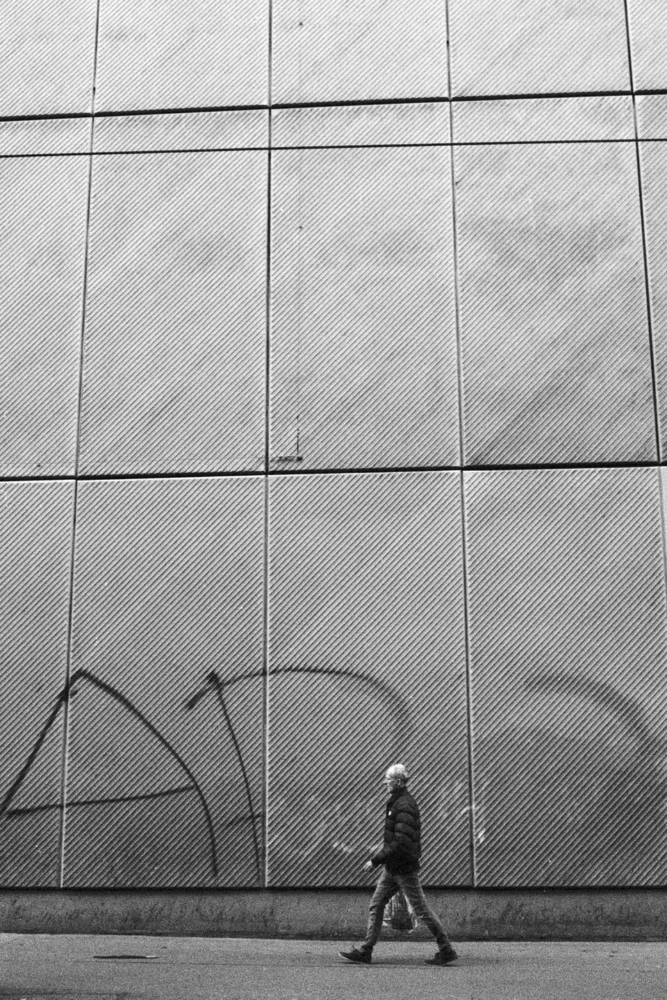 A man walks past a textured wall with graffiti on a street.