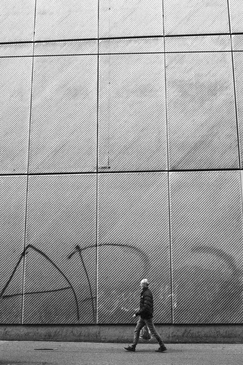 A man walks past a textured wall with graffiti on a street.