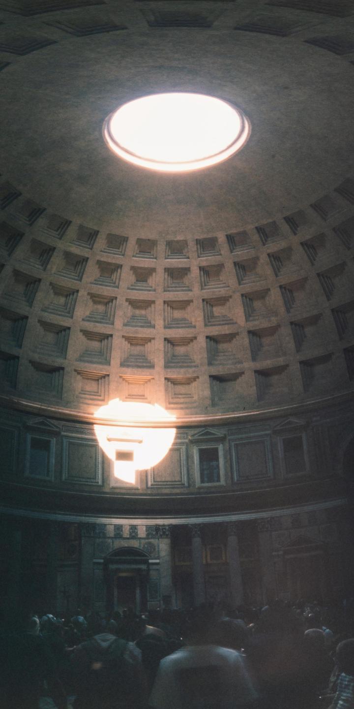 A crowd of people stands inside the Pantheon, illuminated by a circular opening in the domed ceiling.